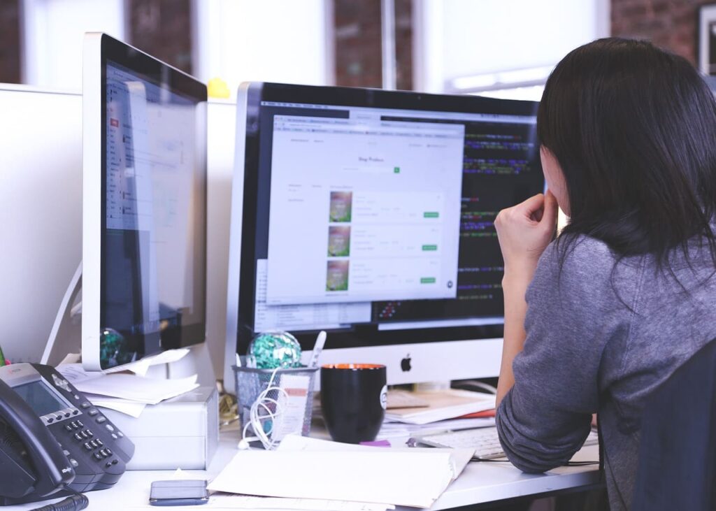 Una mujer sentada en un escritorio con dos monitores mientras trabaja en diseño web.